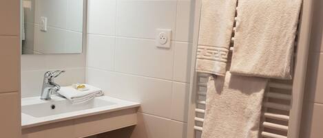 Un baño con lavamanos blanco, espejo y toallero con toallas.