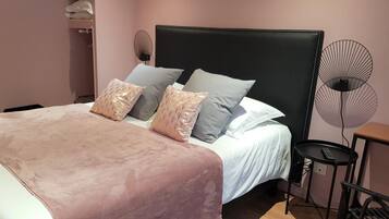 Un lit bien fait, avec une tête de lit noire, plusieurs oreillers et une table de chevet sur laquelle se trouve un ventilateur.