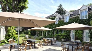 Un espace extérieur aménagé en terrasse, avec des tables et des chaises, ombragé par de grands parasols et entouré de verdure.