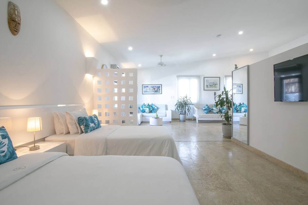 Une chambre d’hôtel moderne avec deux lits, un grand miroir, un téléviseur à écran plat et une plante en pot.