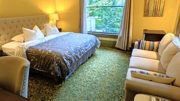 A hotel room with a large bed, a sofa, a chair, and a window with a view of trees.