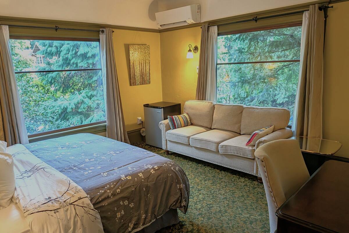Une chambre d’hôtel avec un lit, un canapé, une petite table et une fenêtre donnant sur des arbres.