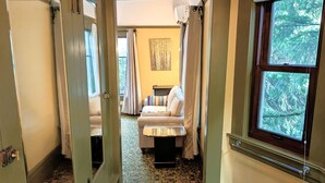 A hallway leading to a bedroom with a bed, a nightstand, and a window with a view of trees. - Evermore Guesthouse (Portland)