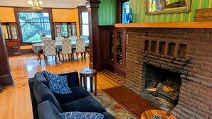 A cozy living room with a fireplace, a sofa with patterned cushions, a dining area with chairs, and a bookshelf. - Evermore Guesthouse (Portland)