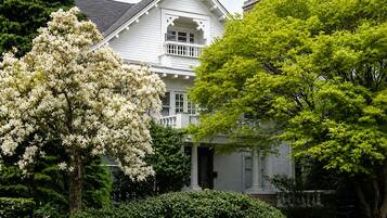 A two-story house with a porch, surrounded by lush greenery and flowering trees.