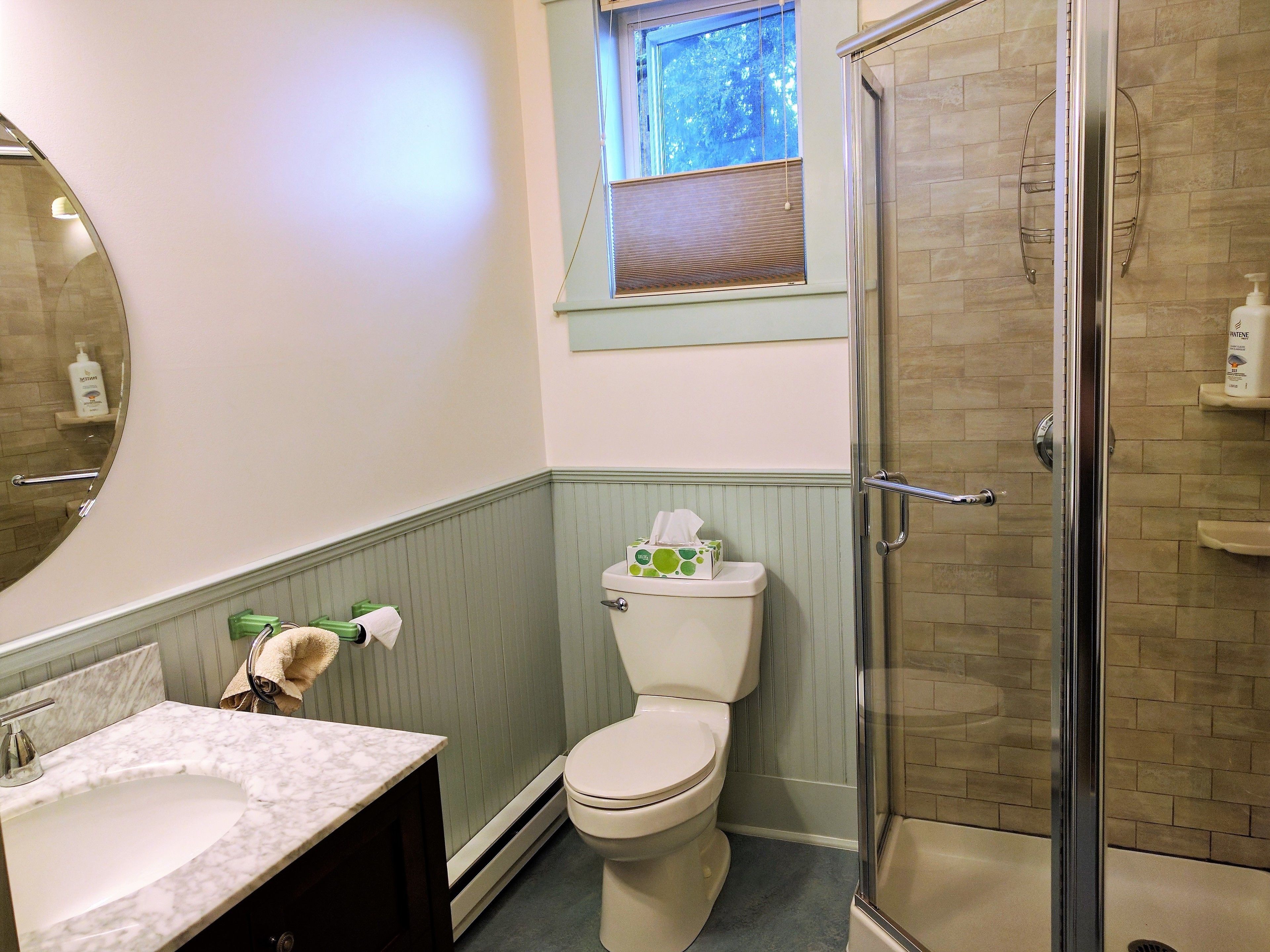A bathroom with a marble sink, a toilet, a glass shower enclosure, and a window above the toilet.