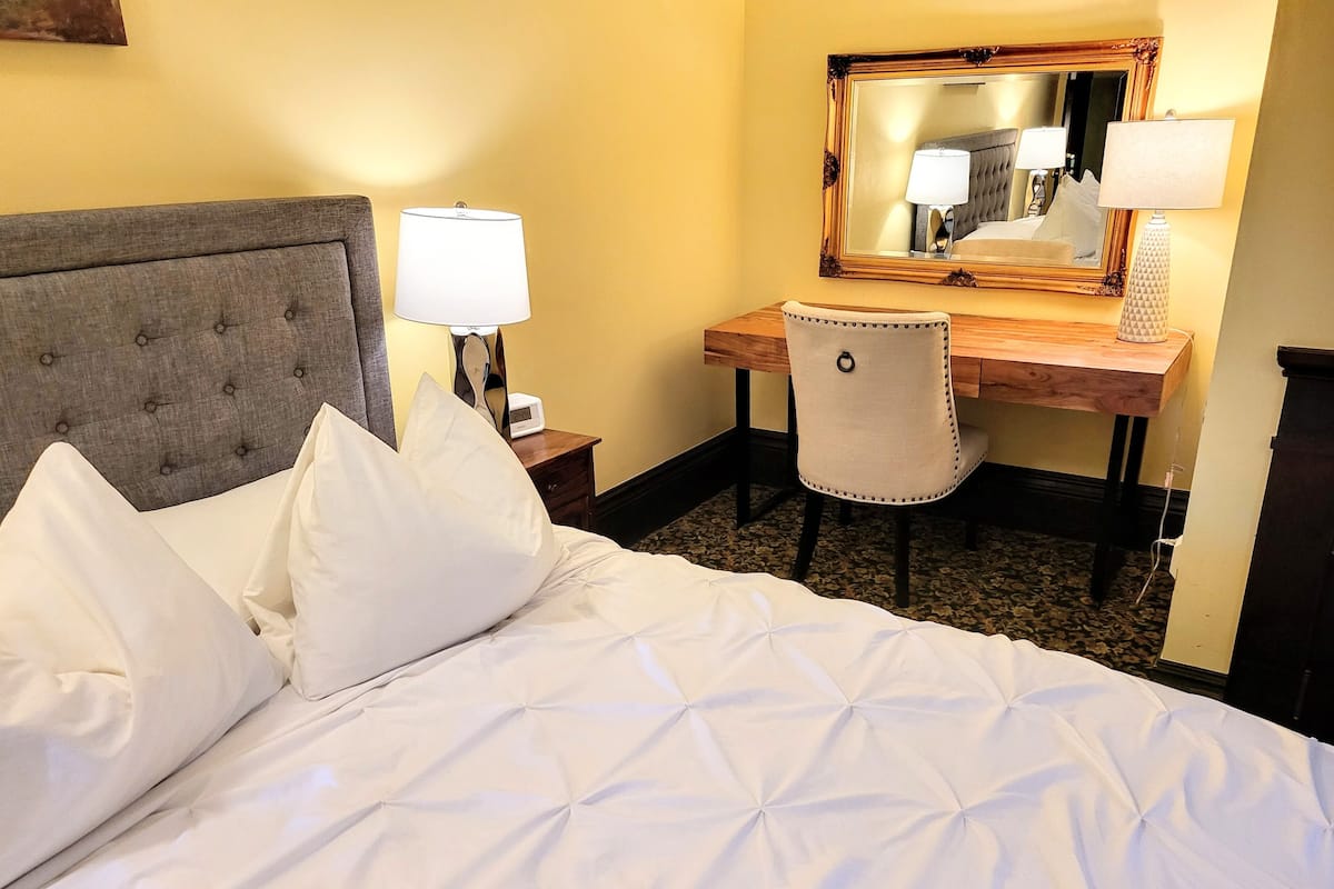 Une chambre d’hôtel avec un lit, un bureau, une chaise, un miroir et une lampe.