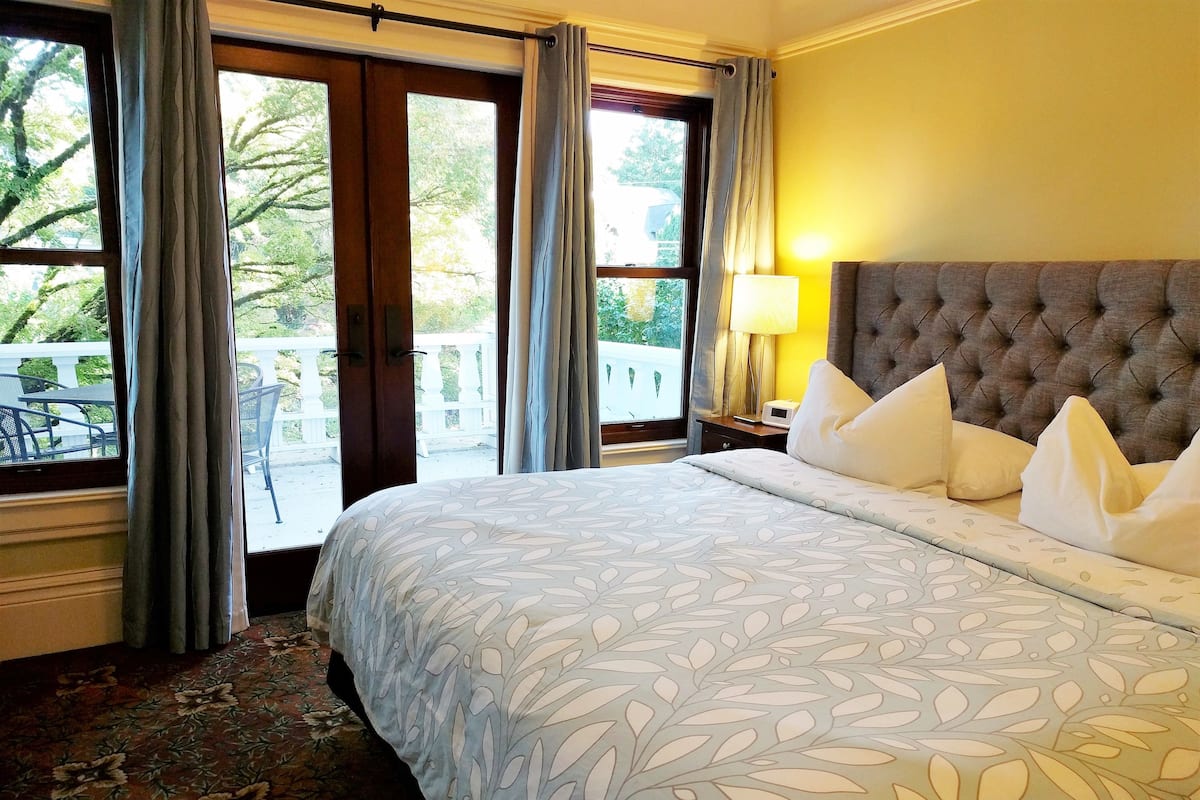 Une chambre d’hôtel avec un grand lit, une tête de lit capitonnée et une vue sur l’extérieur grâce à une grande fenêtre.
