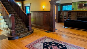 A grand staircase with ornate railings, a chandelier, and a patterned rug on a wooden floor. - Evermore Guesthouse (Portland)