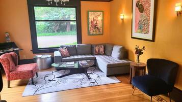 Een woonkamer met een bank, fauteuils, een salontafel en een kroonluchter. Er is een raam met uitzicht op groen.
