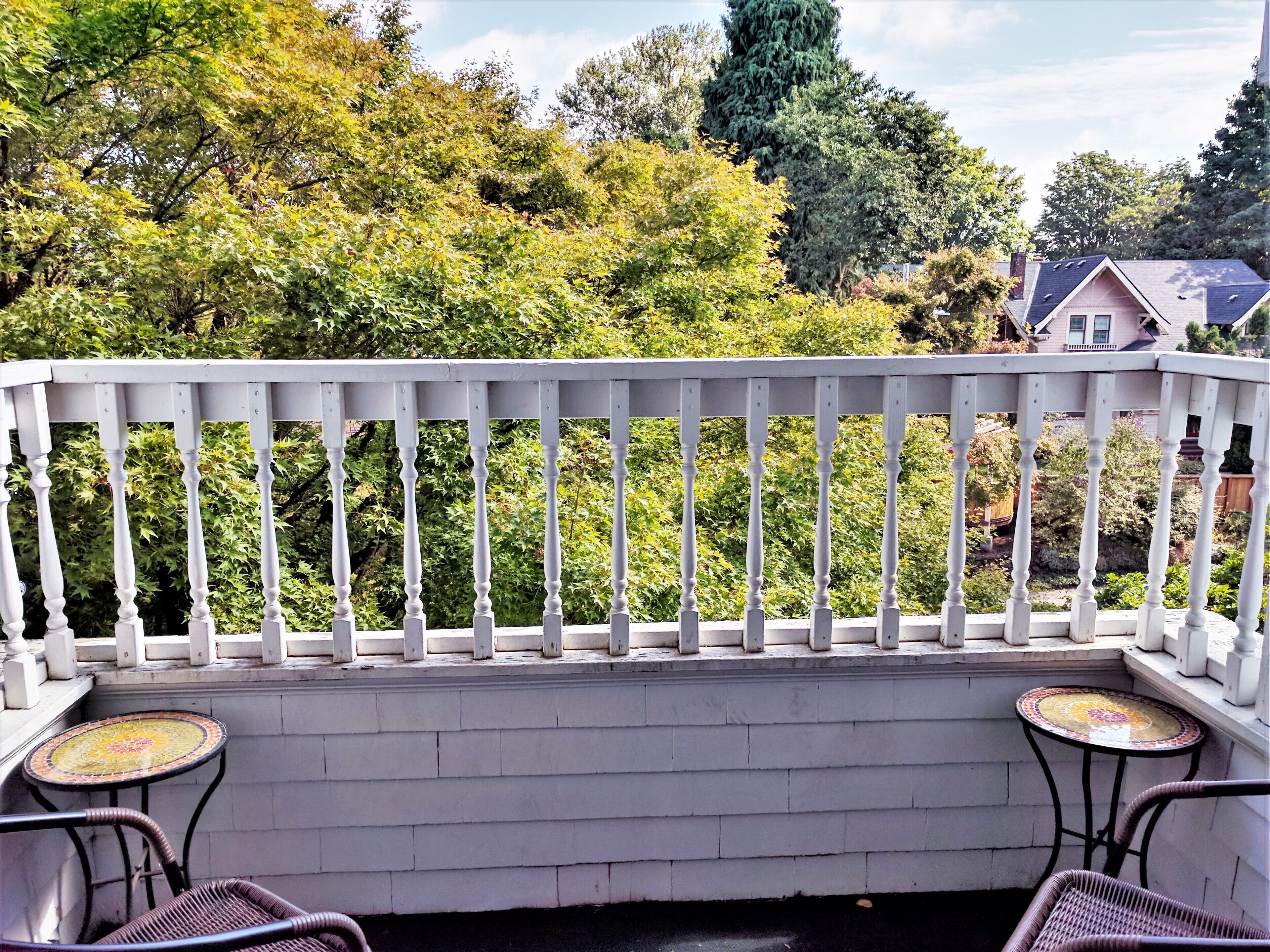 A balcony with a white railing, two wicker chairs, and a small round table with a mosaic top.