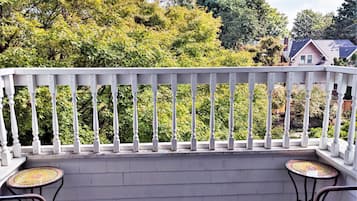 A balcony with a white railing, two wicker chairs, and a small round table with a mosaic top.