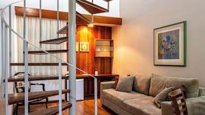 A staircase with wooden steps and metal railings, a beige sofa with cushions, a small table with a lamp, and a framed abstract painting on the wall. - Hotel Dan Inn São José do Rio Preto By Nacional Inn  (São José do Rio Preto)