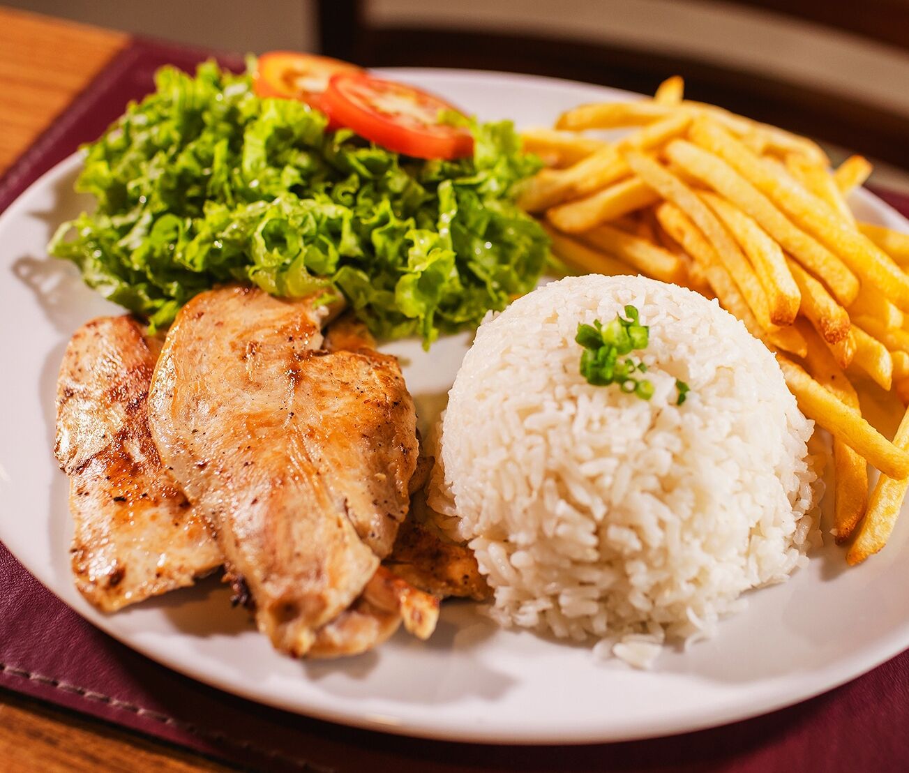 Een bord met gegrilde kip, rijst, friet en een salade van sla en tomaat.