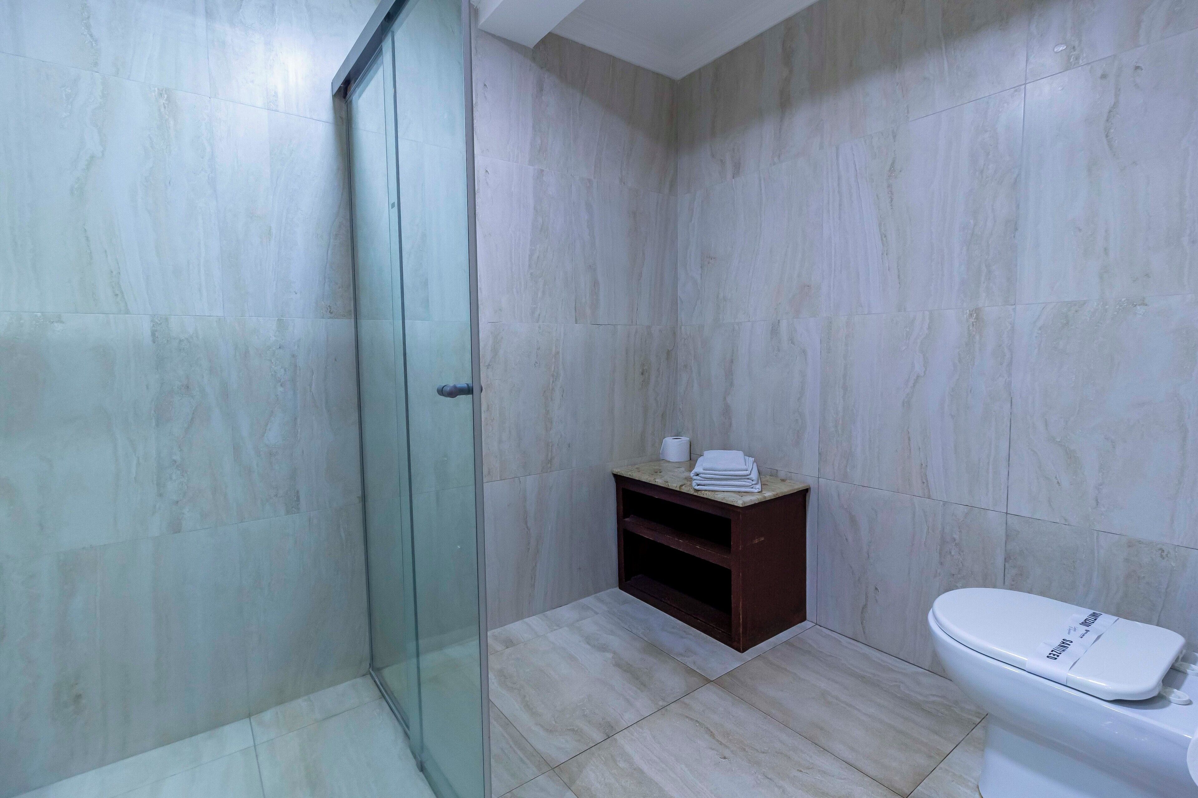 A bathroom with a glass shower enclosure, a toilet, and a small wooden cabinet with toiletries.