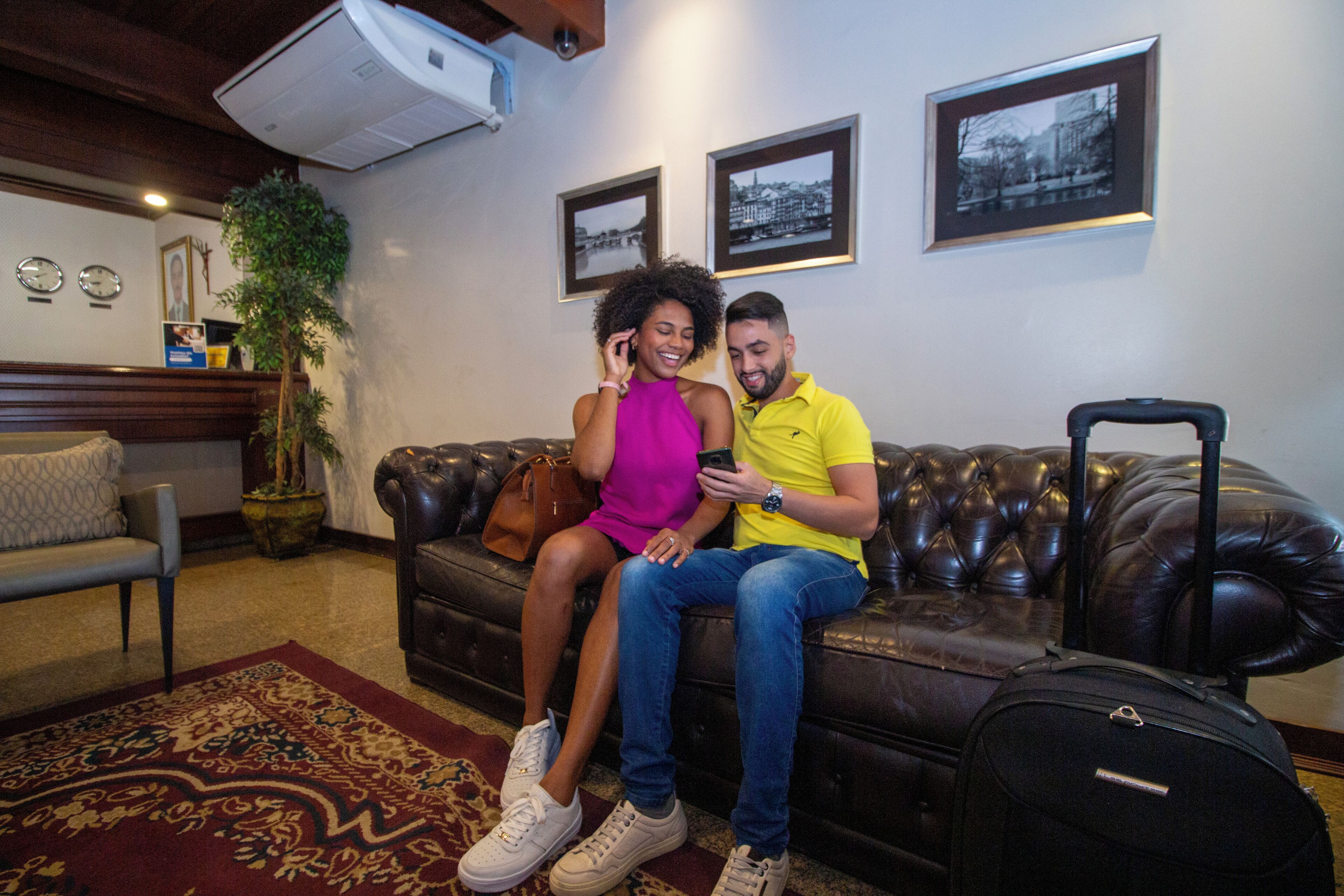 Una pareja sentada en un sofá de cuero en una habitación con una planta grande en maceta, un reloj y cuadros en la pared.