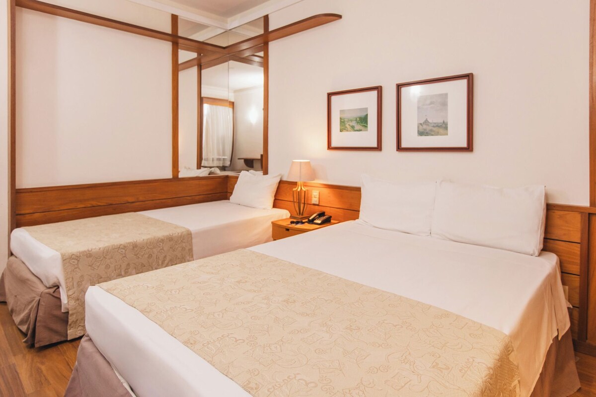 Een hotelkamer met twee bedden, een nachtkastje met een lamp en twee ingekaderde foto's aan de muur.