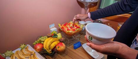A buffet table with sliced bananas, apples, and a fruit salad.