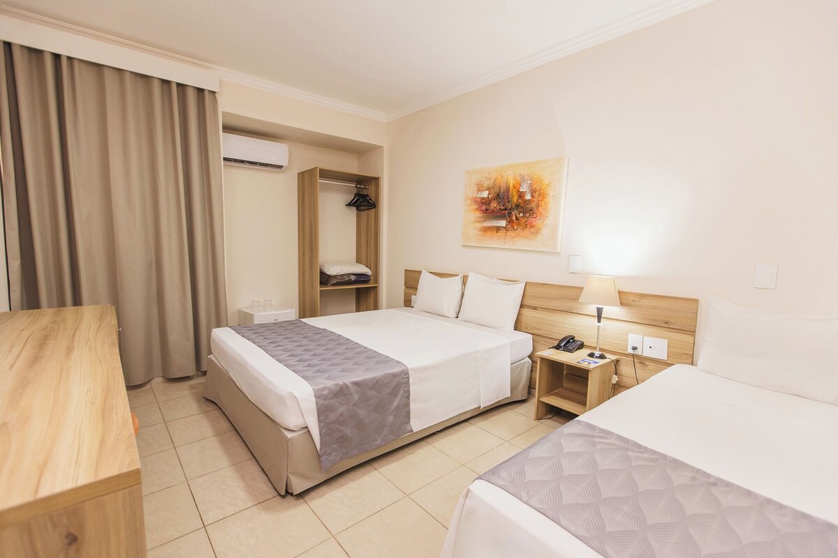 Een hotelkamer met een bed, nachtkastje, lamp en een schilderij aan de muur.