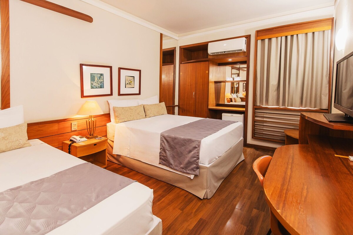 Een hotelkamer met twee bedden, een bureau, een televisie, een kledingkast en een spiegel.
