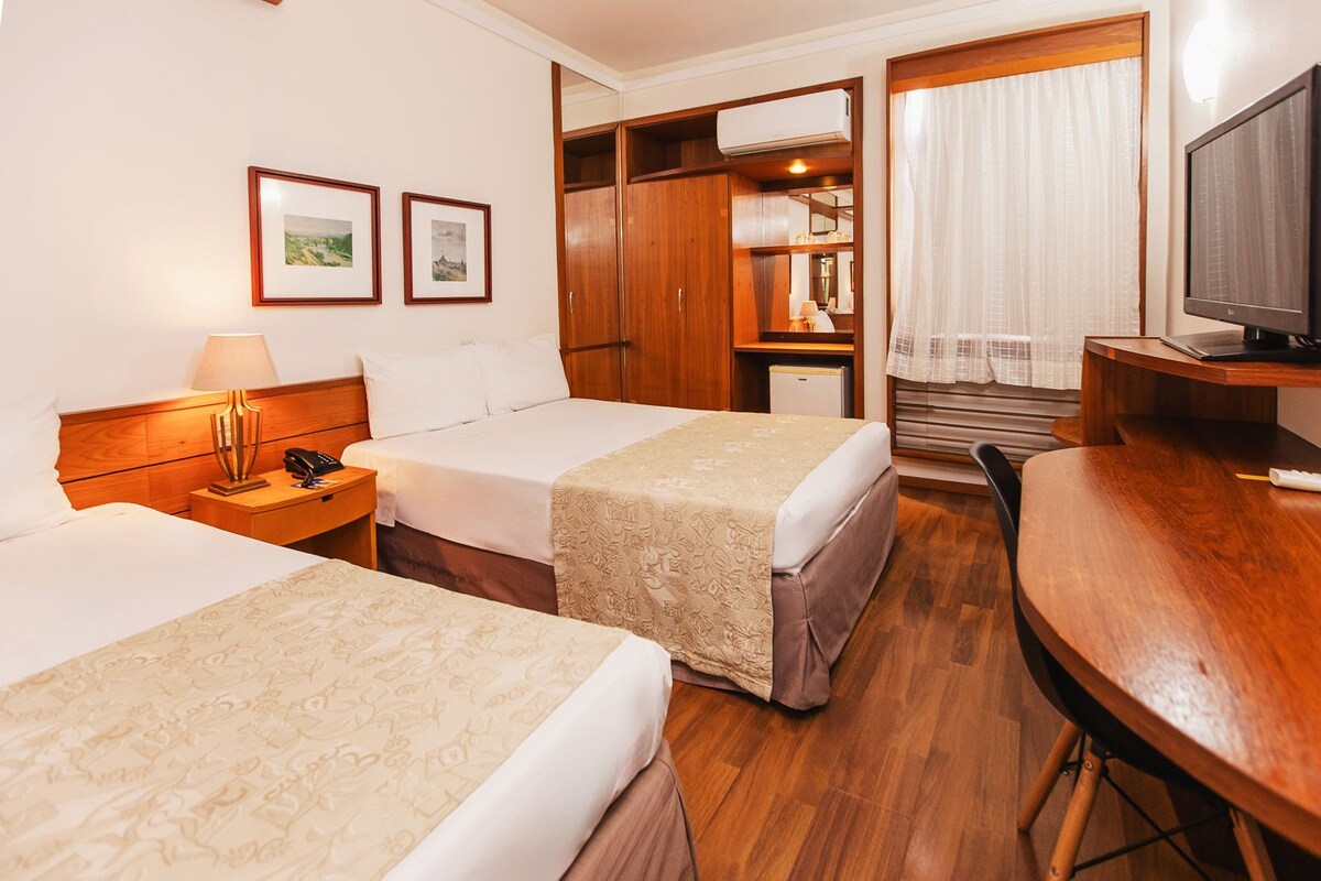 A hotel room with two beds, a desk, a television, and a wardrobe.