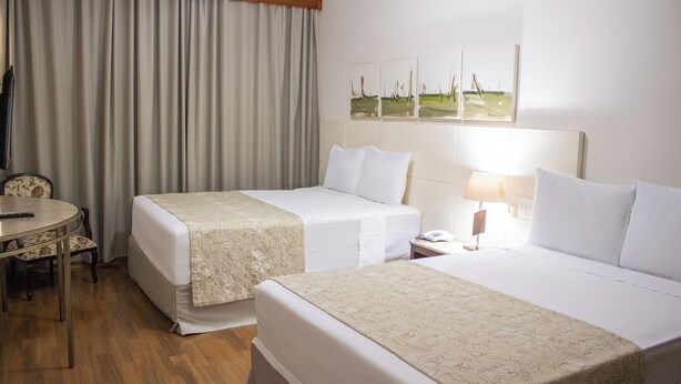 A hotel room with two beds, a dining table, and a painting on the wall.
