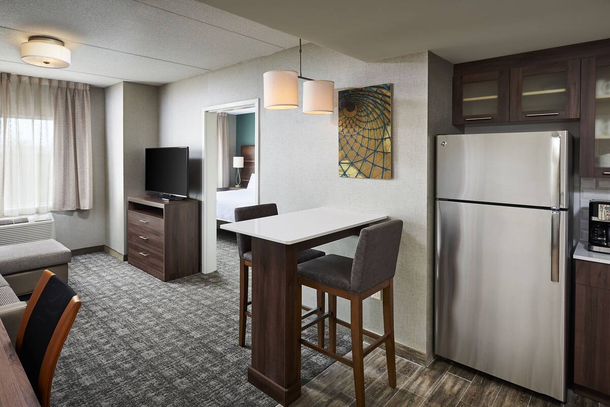 Une chambre d’hôtel équipée d’une kitchenette, d’un coin repas, d’une télévision, d’un canapé et d’une fenêtre avec des rideaux.