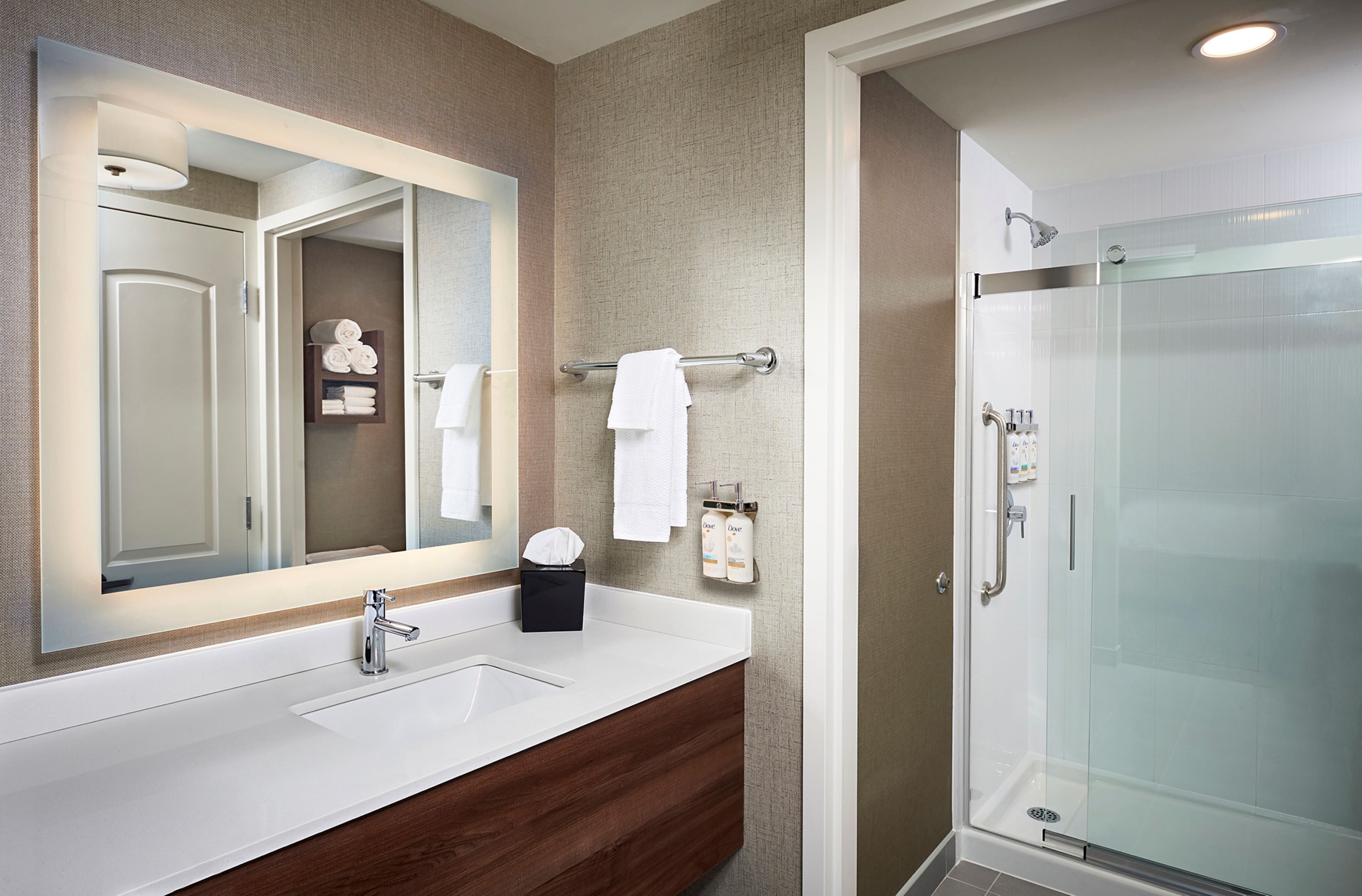 A modern bathroom with a large mirror, a white sink, a glass shower enclosure, and a towel rack with folded towels.