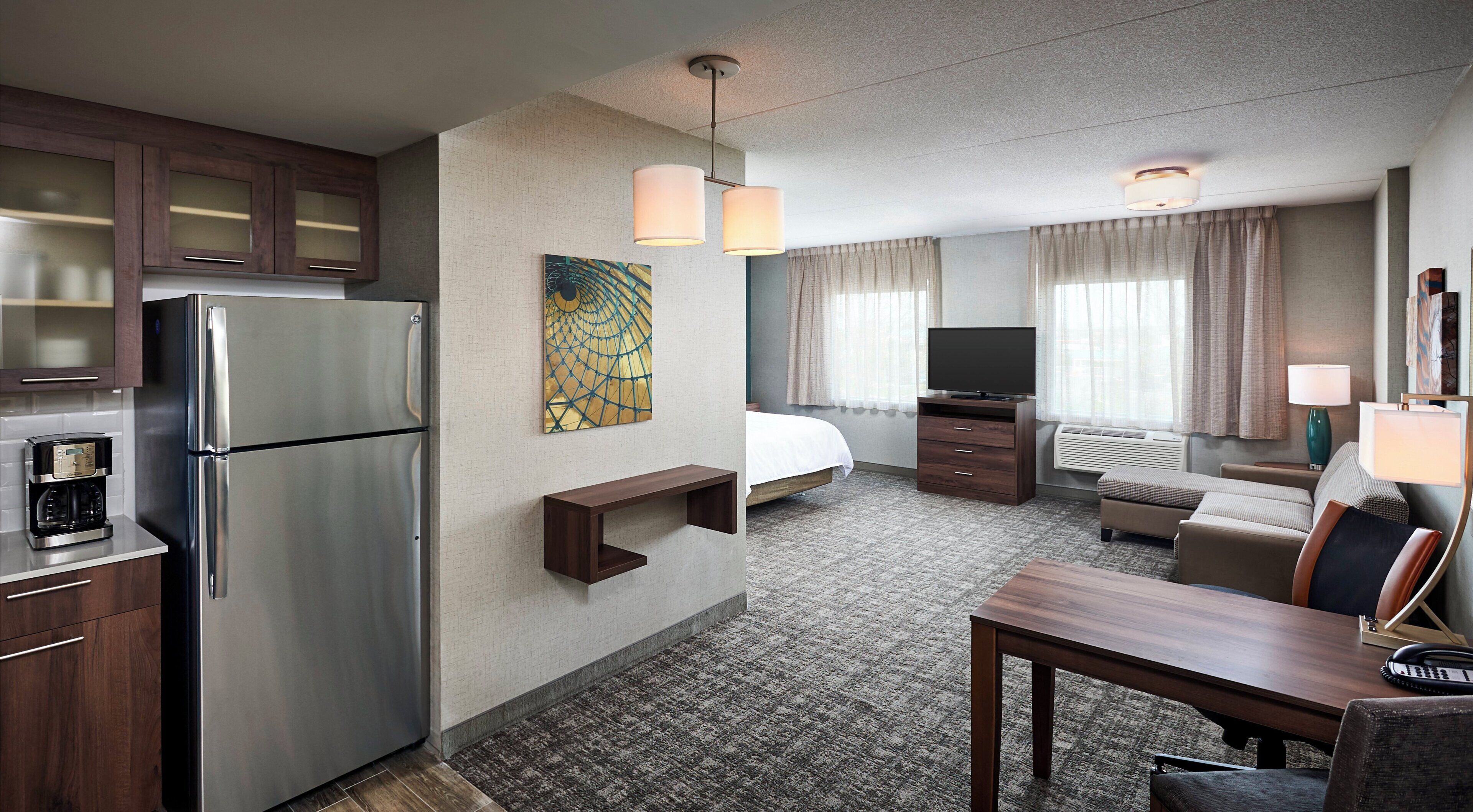 A hotel room with a kitchenette, a bed, a seating area, and a television.
