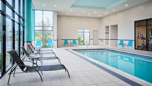 Une piscine intérieure moderne avec des murs en verre transparent, des chaises bleues et un sol carrelé.