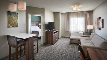 A hotel room with a dining table, a sofa, a TV, and a window with curtains.