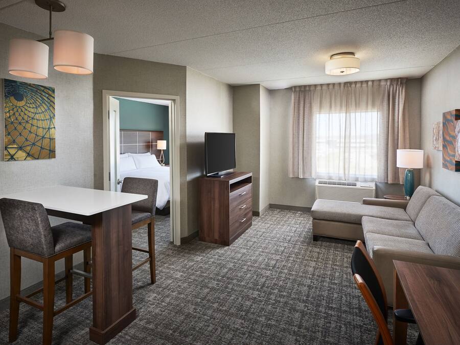A hotel room with a dining table, a sofa, a TV, and a window with curtains.