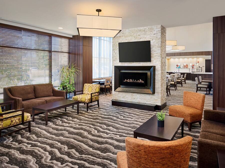 A modern hotel lobby with a fireplace, comfortable seating, and a dining area in the background.