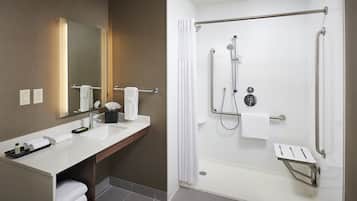 Een moderne badkamer met een grote spiegel, een witte wastafel en een inloopdouche met handgrepen.