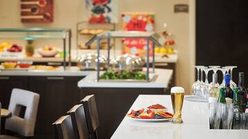 A dining area with a buffet setup, including a plate of nachos, a glass of beer, and a variety of bottles and glasses on the table.