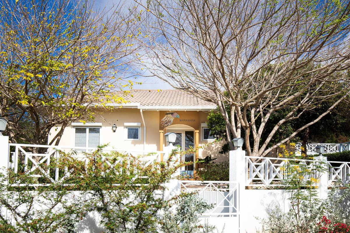 A two-story house with a tiled roof, a white fence, and a tree in the foreground.