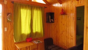 A wooden room with a window, a small table, a chair, and a shelf with a red object. - Cabanas Patricia en Horcon (Puchuncavi)