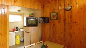 A compact kitchen with wooden walls, a small refrigerator, a microwave, and a table with chairs. - Cabanas Patricia en Horcon (Puchuncavi)