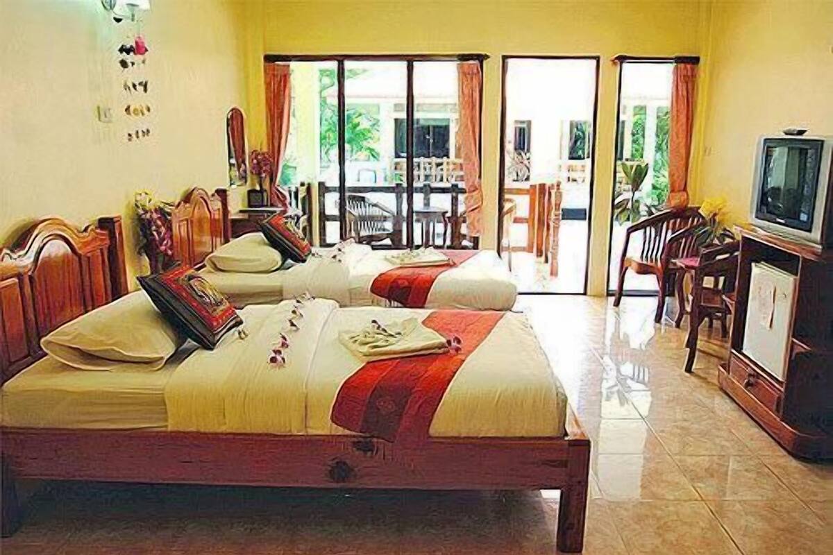 A hotel room with two beds, a TV, and a balcony with chairs.