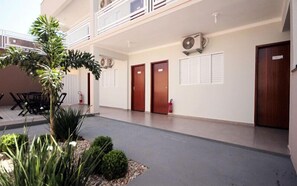 Un couloir d’hôtel avec un toit plat, deux portes en bois, un extincteur et un climatiseur fixé au mur.