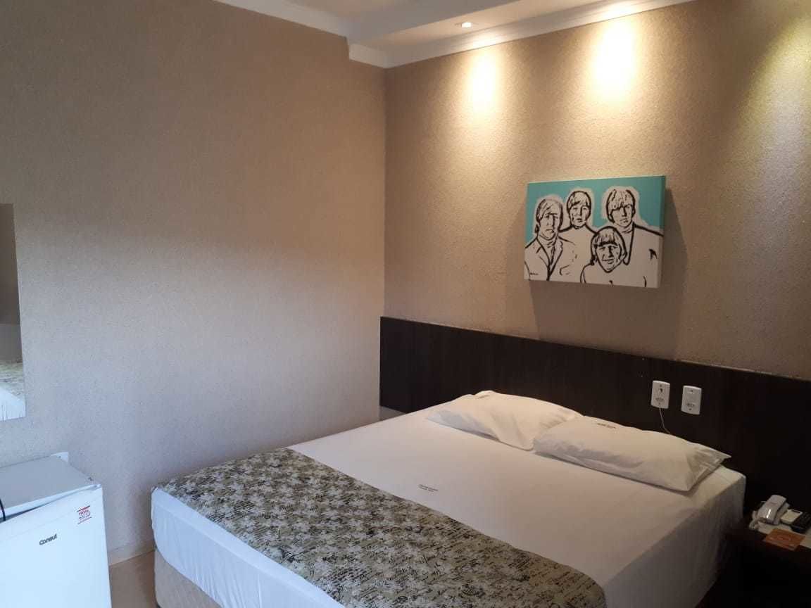 A hotel room with a bed, a small desk, a wall-mounted artwork, and a light fixture.