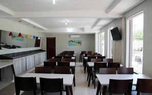 Un grand espace dédié à la salle à manger, avec plusieurs tables et chaises, un comptoir doté d’un évier et une grande fenêtre qui laisse entrer la lumière naturelle.