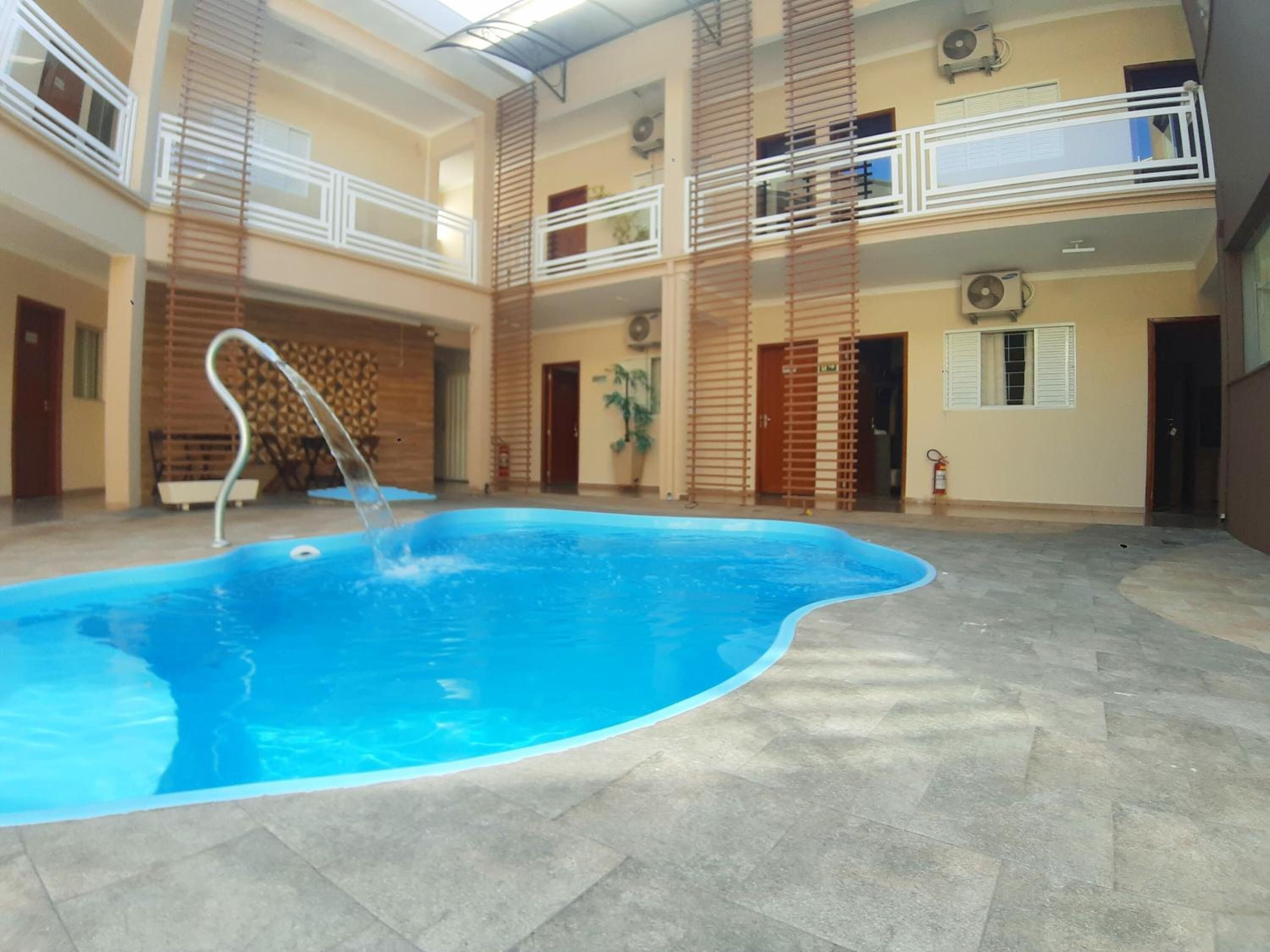 An indoor swimming pool with a clear water feature, surrounded by a tiled floor and a multi-level balcony with railings.