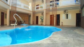 An indoor swimming pool with a clear water feature, surrounded by a tiled floor and a multi-level balcony with railings.
