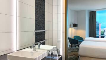A hotel room with a large bed, a bathroom with a sink and mirror, and a view of the city through the window.