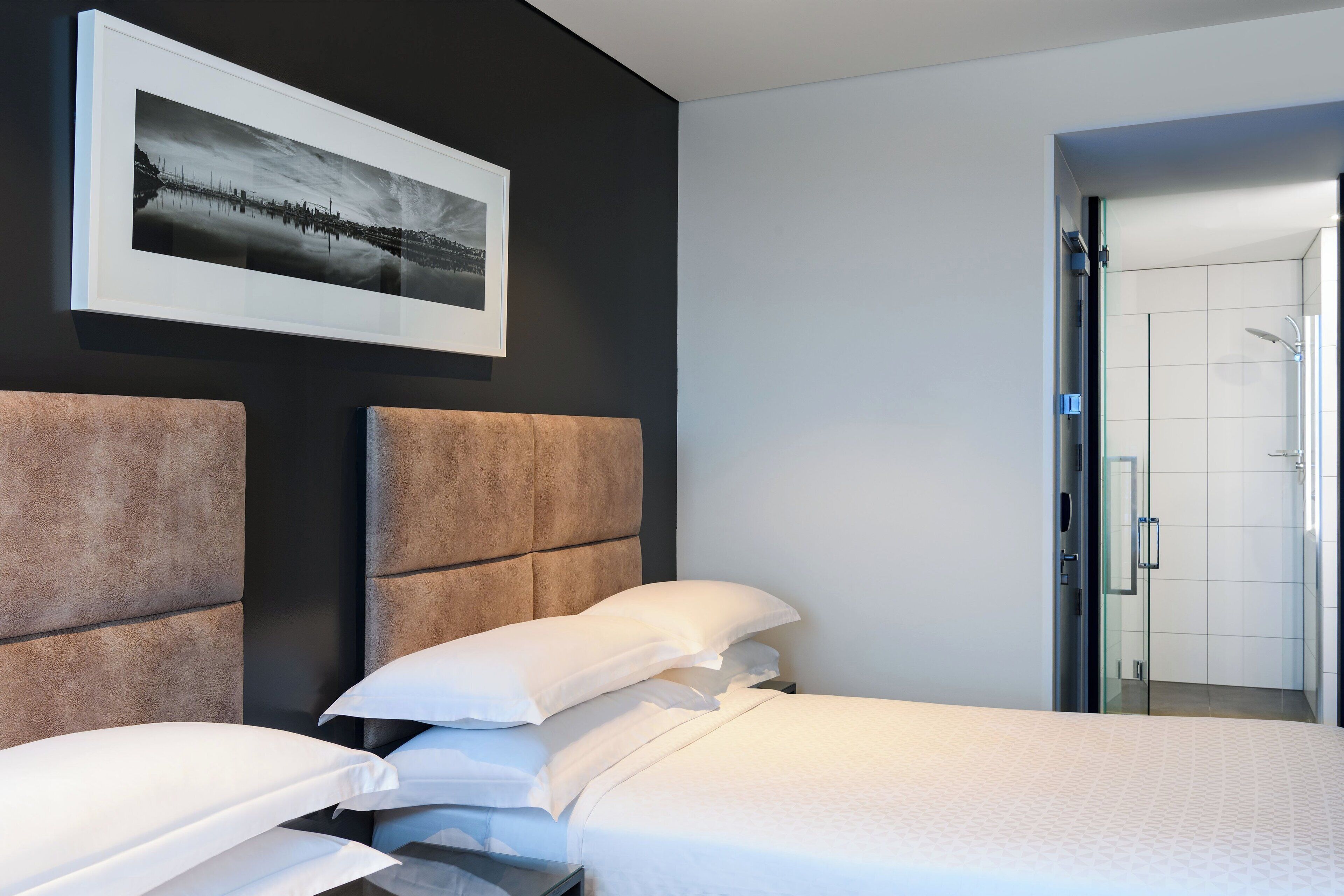 A modern hotel room with a large bed, a headboard, a framed picture on the wall, and a bathroom visible through an open door.