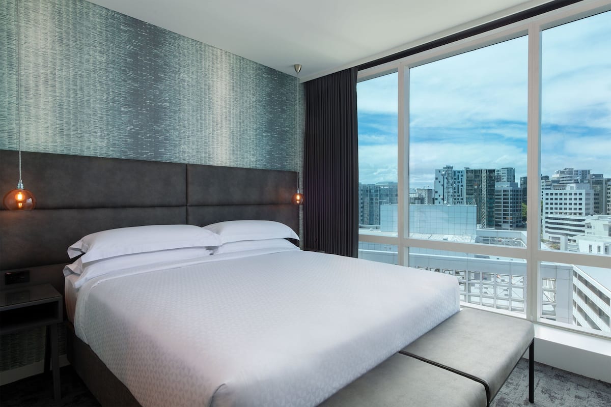A modern hotel room with a large bed, a view of the cityscape, and a textured wall.