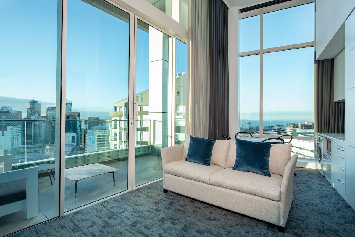 A modern living room with a sofa, a coffee table, and a view of the city through large windows.