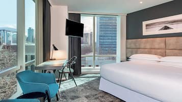 Una habitación de hotel moderna con una cama grande, un escritorio con silla, televisión y vistas a la ciudad.