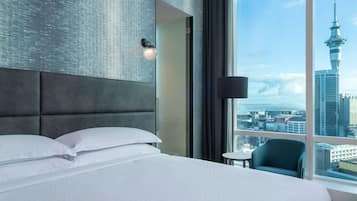 Hotelkamer met een groot bed, hoofdeinde, bedlampje en uitzicht op een stadsbeeld met een toren.